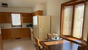 A compact kitchen with wooden cabinets, a refrigerator, a microwave, and a dining table with chairs. - Hill Cottage (Park River)