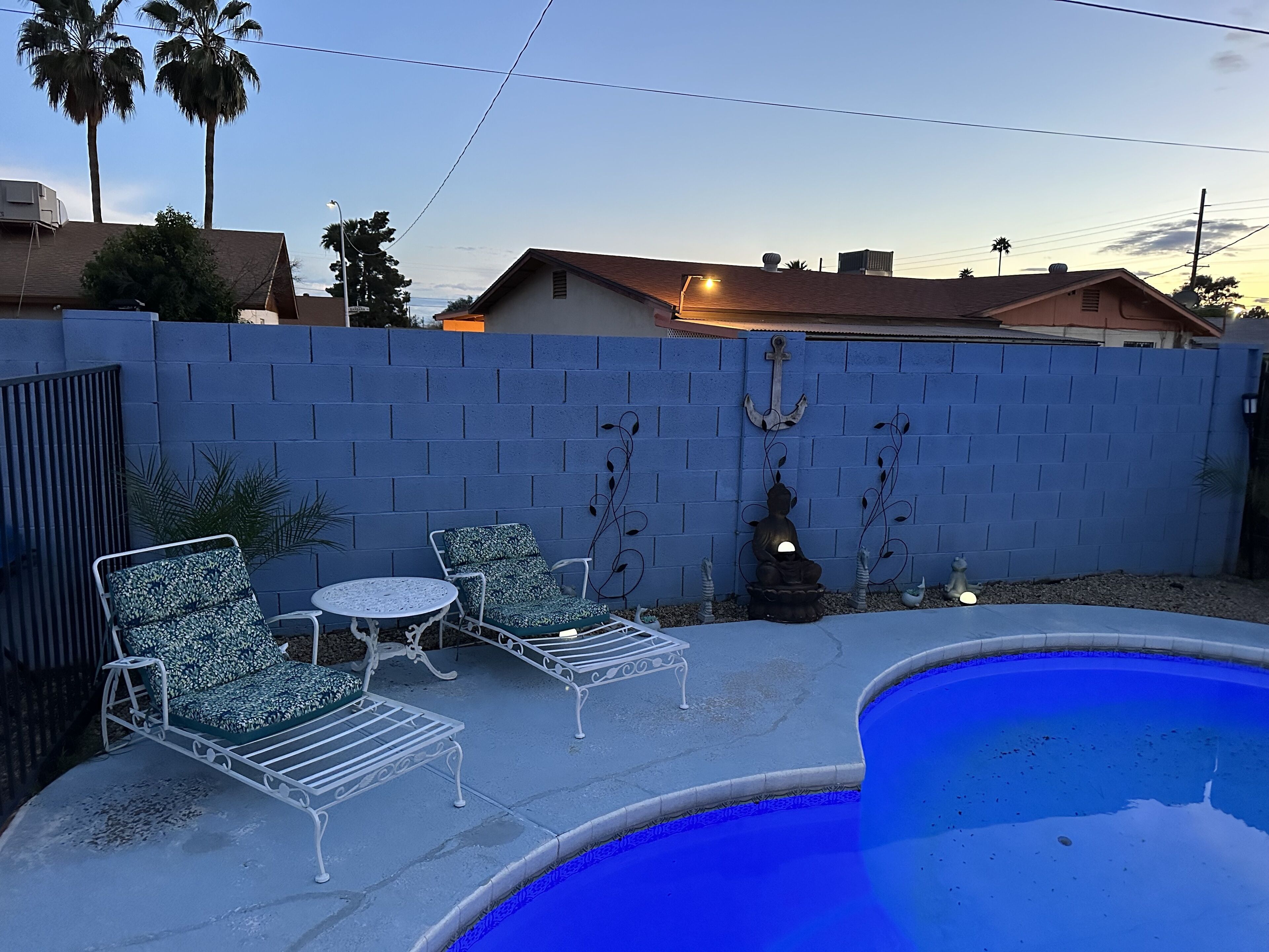 Ein Garten mit Swimmingpool, zwei Liegestühlen, einem kleinen Tisch und einer dekorativen Buddha-Statue.