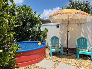 A backyard with a red inflatable pool, two turquoise chairs, and a decorative umbrella.