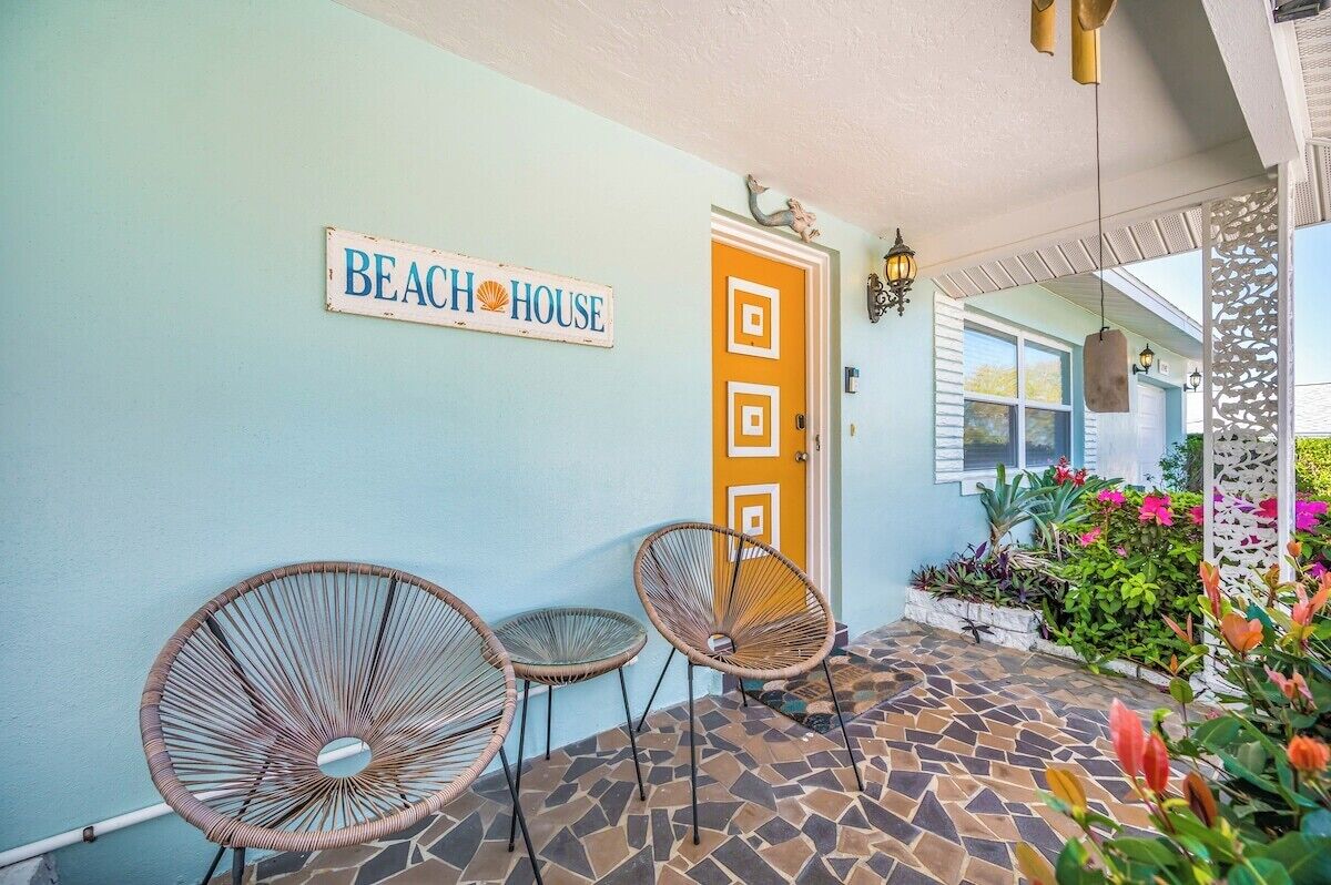 Una entrada con temática de playa, un letrero, dos sillas de mimbre y un patio con baldosas.