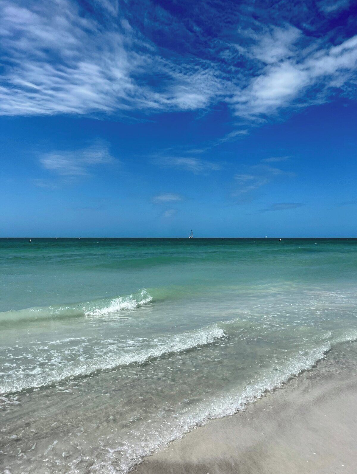 A beach with clear water and a distant boat.