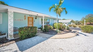Uma propriedade à beira-mar com uma placa que diz 'BEACH HOUSE', uma palmeira e um caminho de acesso de brita.
