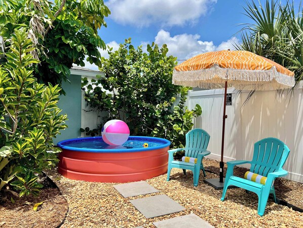 A backyard with a small inflatable pool, two turquoise chairs, and an umbrella.