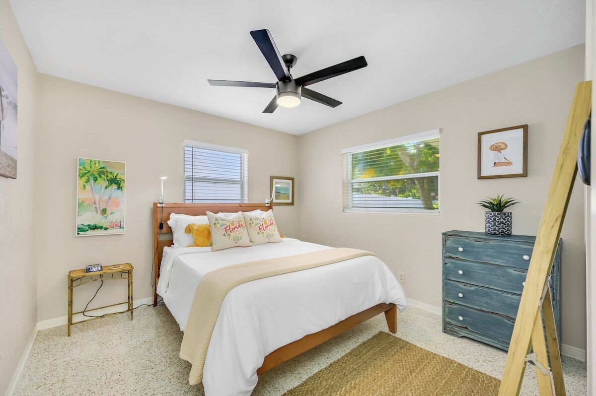 A bedroom with a bed, a ceiling fan, a dresser, and artwork on the walls.