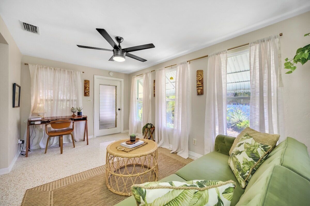 A living room with a ceiling fan, a green sofa, a round wicker coffee table, and a desk with a chair.