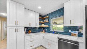 Uma cozinha moderna com armários brancos, lava-louças de aço inoxidável e painel de azulejos azuis.