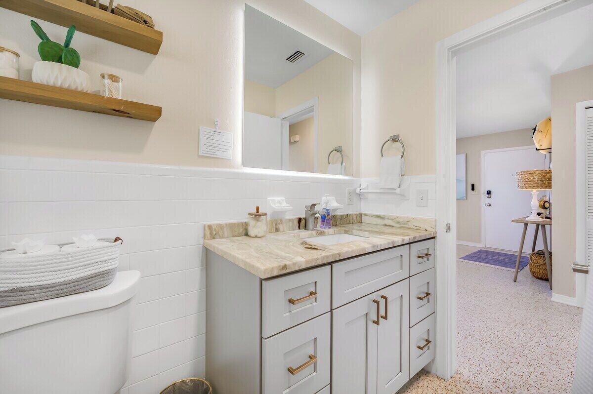 Un baño moderno con muebles blancos, encimera de mármol y un espejo grande.