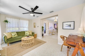 A living room with a green sofa, a round coffee table, a dining table with chairs, a ceiling fan, and a chandelier. - 5 Minutes to Madeira Beach • Private Cowboy Pool (Seminole)