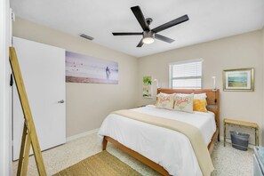 A bedroom with a bed, a ceiling fan, a window, and a painting on the wall.