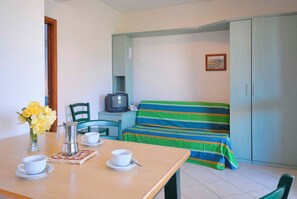 Una habitación con una mesa de madera dispuesta para dos, un sofá con una manta a rayas, un televisor y un armario.