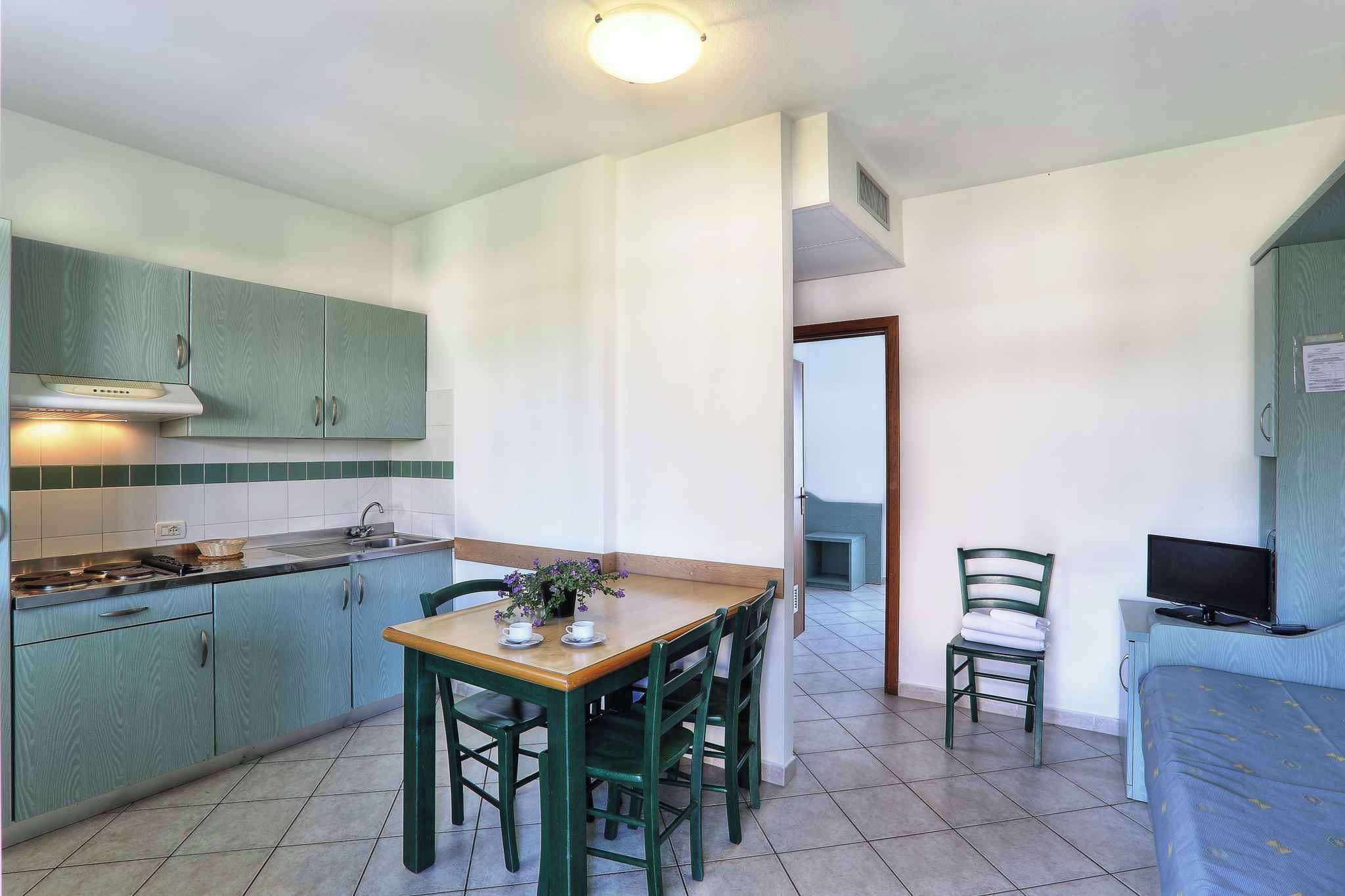 A compact kitchen with green cabinets, a dining table with chairs, and a small TV.