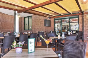 Un espace extérieur aménagé avec des chaises et des tables en osier, un panneau affichant le menu et un cocktail posé sur la table.