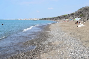 A pebbly beach with umbrellas and people relaxing. - Holiday apartment with air conditioning and outdoor pool (Cecina)