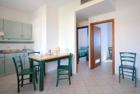Una cocina compacta con zona de comedor, sillas verdes y una mesa pequeña con un florero.