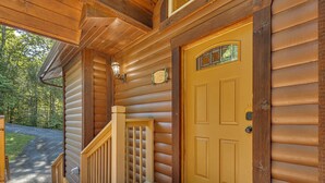 Una cabaña de madera con puerta principal, un porche y una escalera que conduce a la entrada.