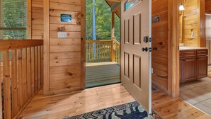 Interior de una cabaña de madera con puerta de madera, un pequeño balcón y vistas del bosque circundante.