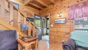 A wooden interior with a staircase, a couch, a lamp, and a door leading outside. - ER81 - Family Making Memories (Pigeon Forge)