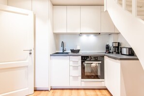 A compact kitchen with white cabinets, a built-in oven, a coffee maker, and a toaster.
