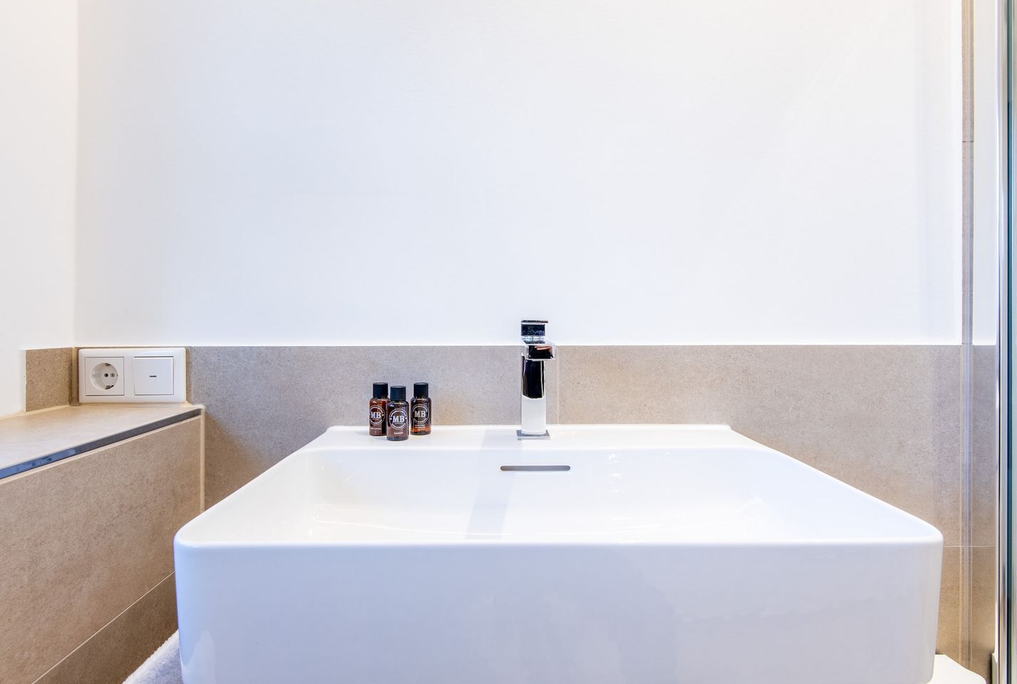 Casa de banho moderna com uma banheira branca grande, uma torneira cromada e três pequenos frascos de produtos de banho na borda.