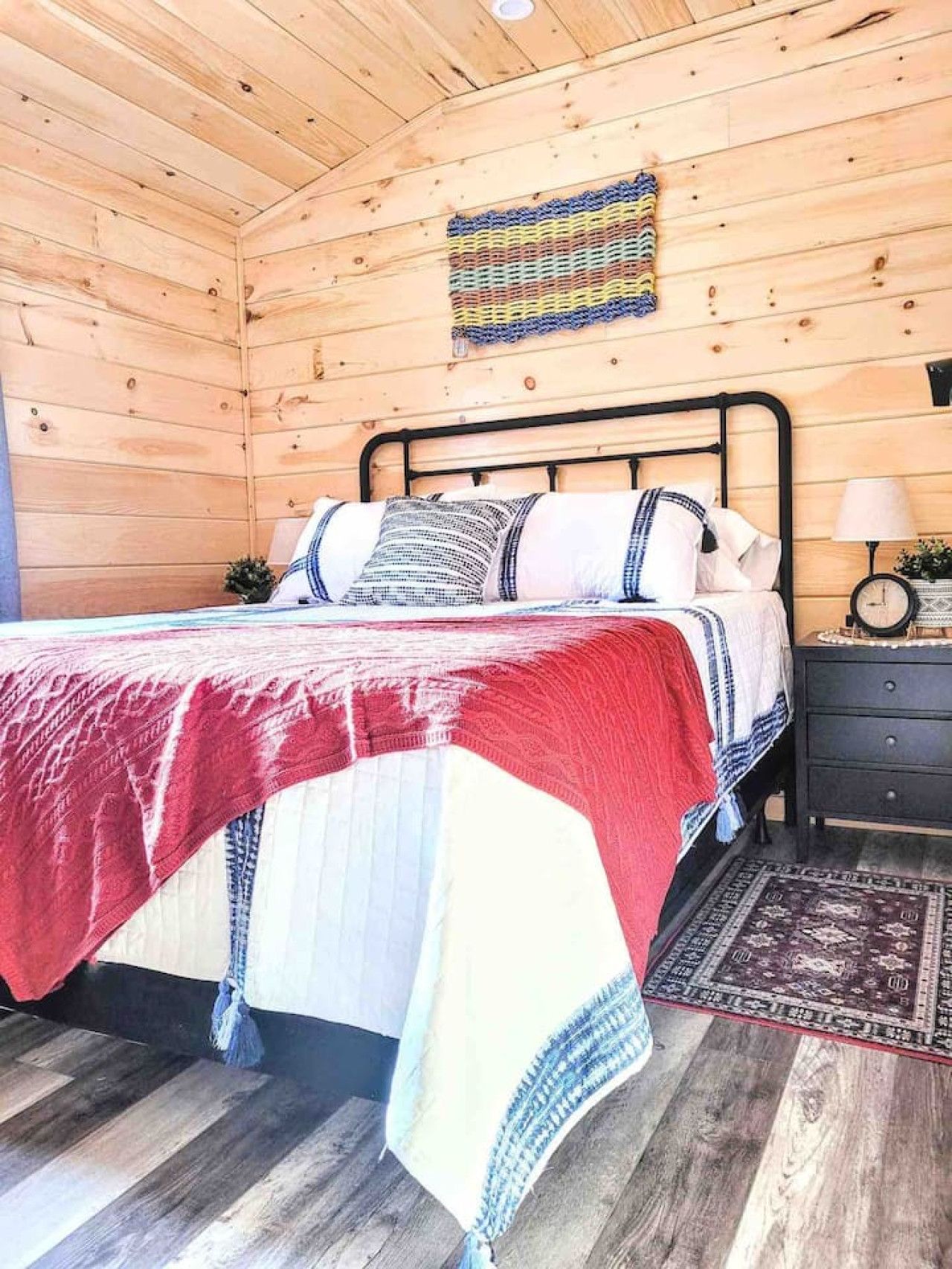 A wooden cabin bedroom with a bed, nightstand, and a wall-mounted clock.