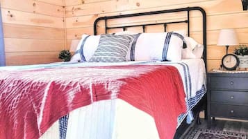 A wooden cabin bedroom with a bed, nightstand, and a wall-mounted clock.