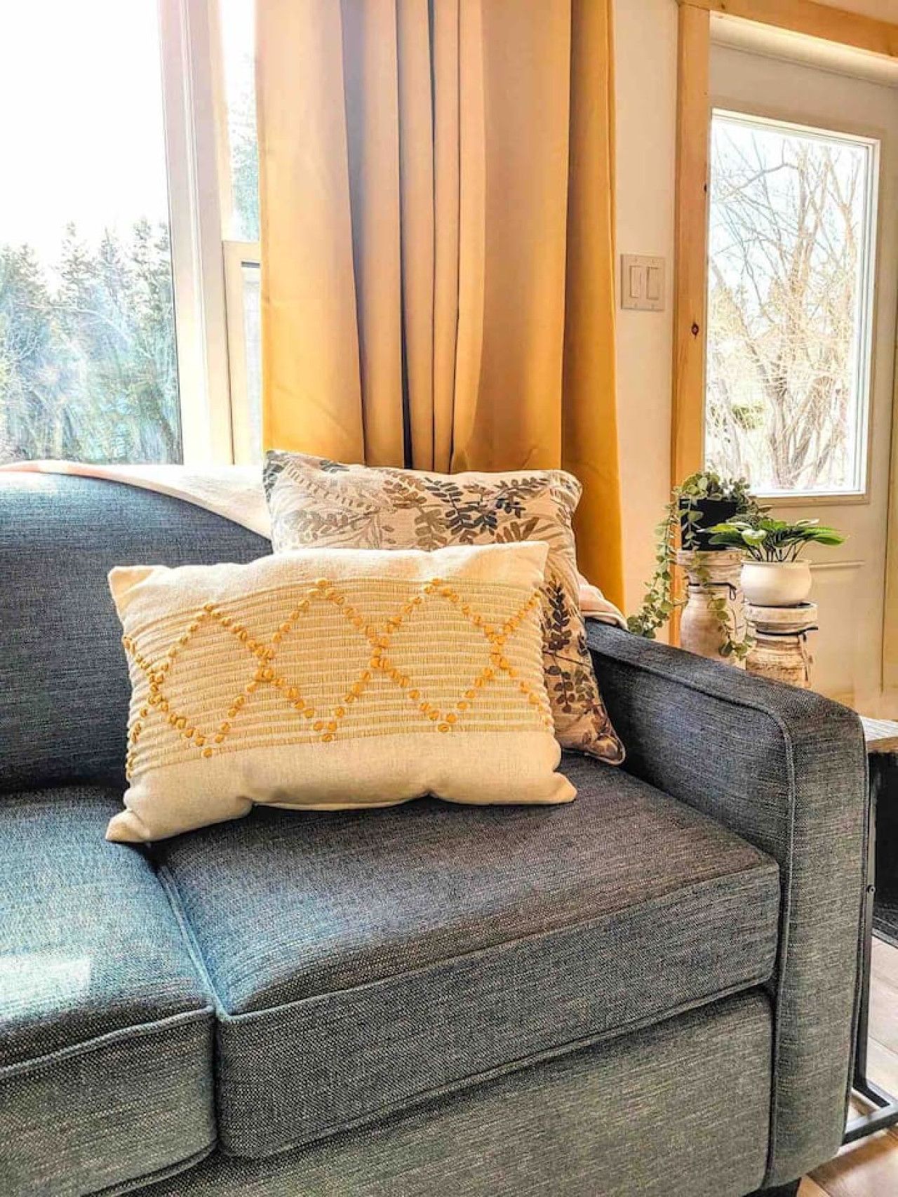 A grey sofa with two decorative pillows, one with a yellow pattern and the other with a floral design.