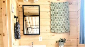 Ein Badezimmer einer Holzhütte mit einem weißen Waschbecken, einem Spiegel, einer Toilette und einem kleinen Mülleimer.