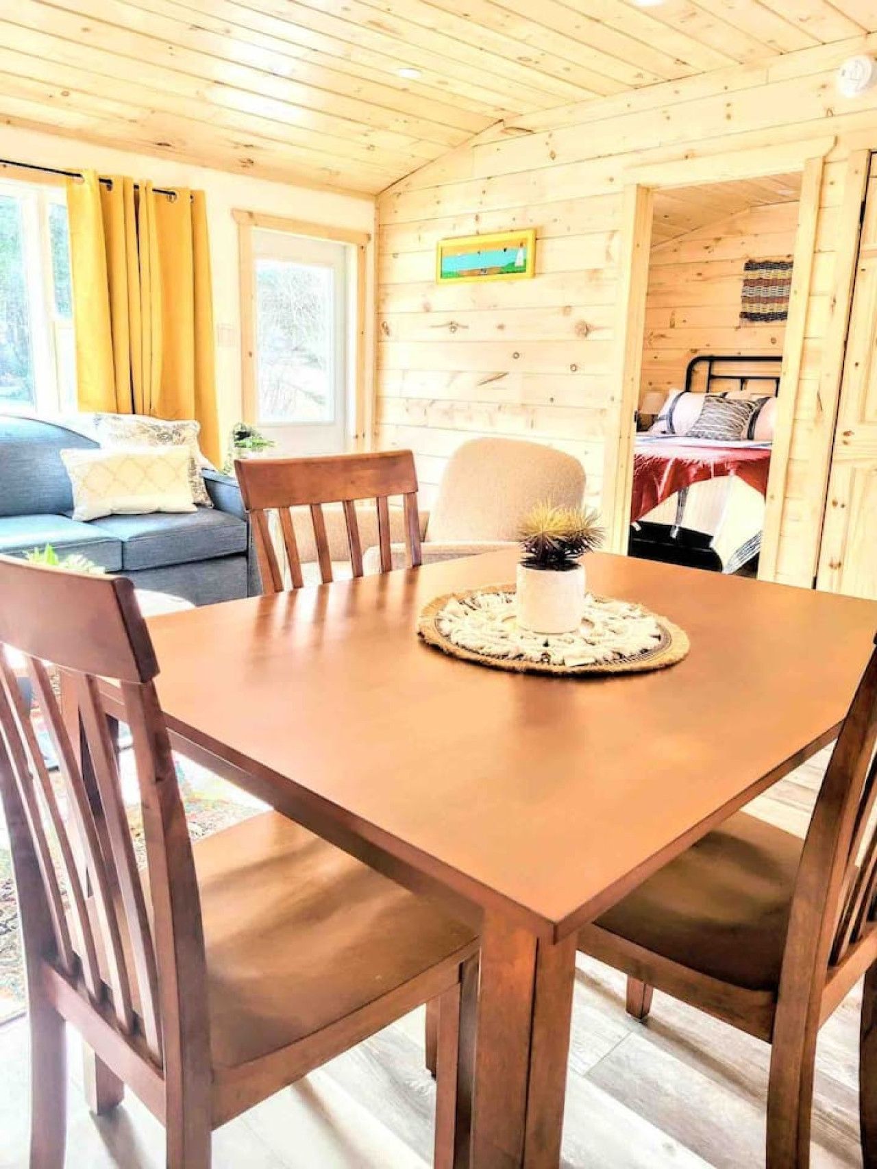 A wooden cabin interior with a dining table, chairs, a sofa, and a bed.