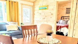 Ein Holzinnenraum mit einem Esstisch, Stühlen, einer Couch und einem Bett.