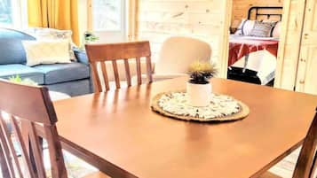 A wooden cabin interior with a dining table, chairs, a sofa, and a bed.