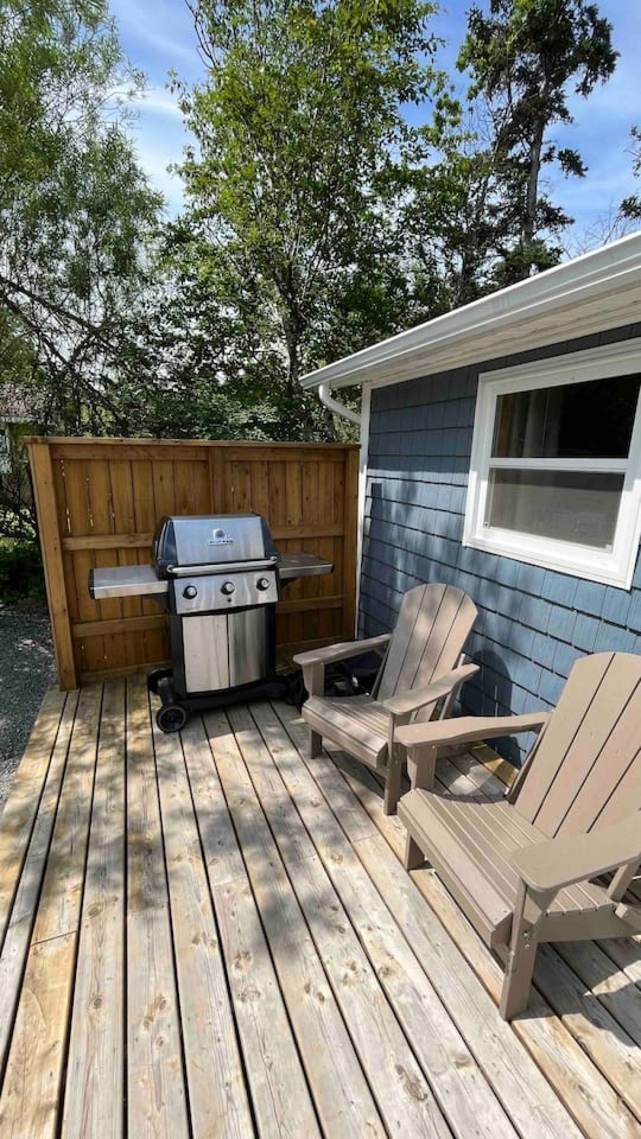 Een houten terras met een barbecue en Adirondack-stoelen.