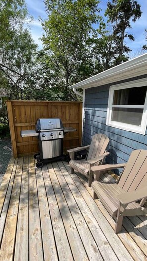 Una terraza de madera con una parrilla y sillones Adirondack.