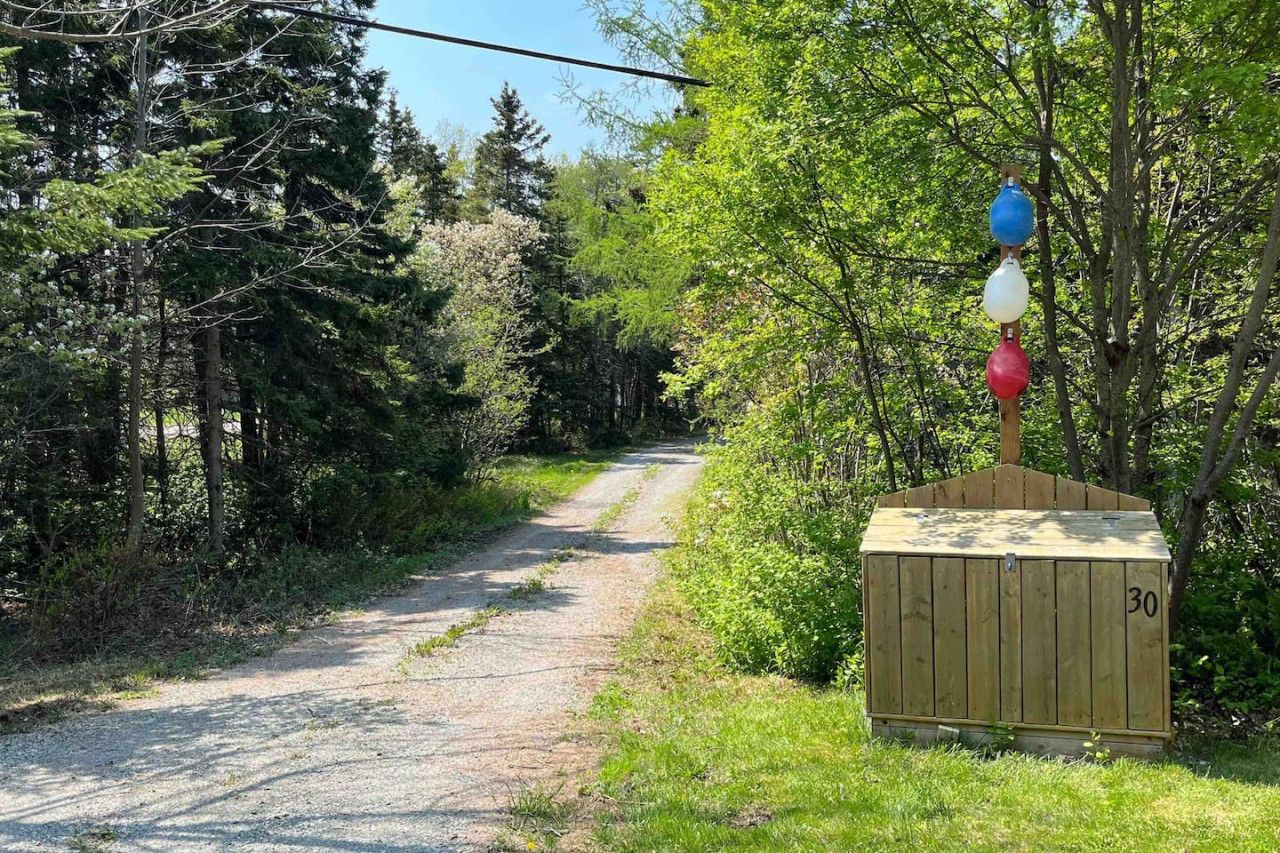 Un chemin de gravier traverse une zone boisée et mène à un abri en bois portant le numéro 30.