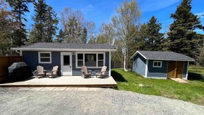 Ein Haus mit einer Veranda, einem kleinen Gartenhaus und einem Grill.