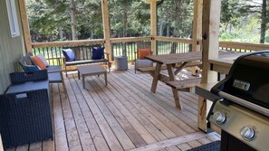 Una terraza de madera con mobiliario exterior, incluyendo una parrilla y zonas de estar.