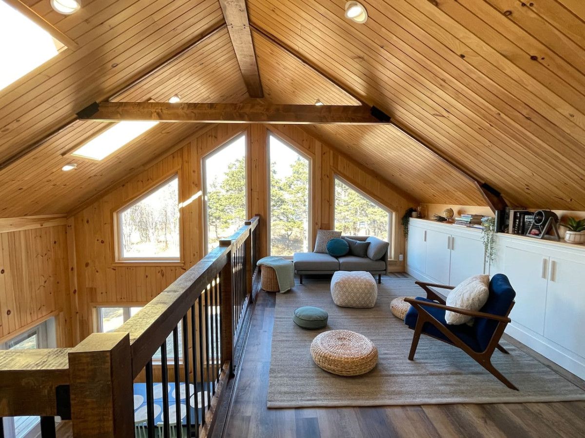 Ein Loft-Zimmer mit schrägem Dach, Holzwänden und einem Balkon.