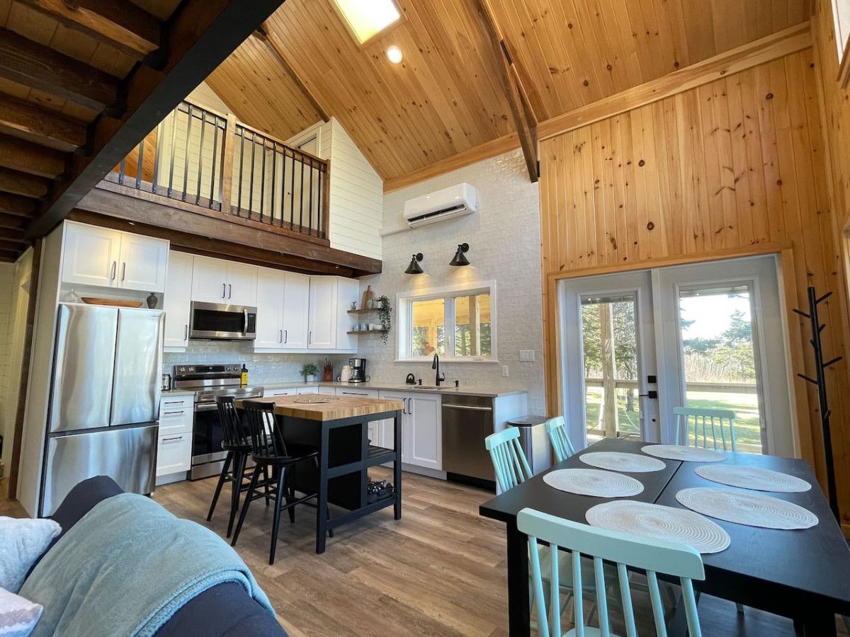 A modern kitchen with a dining area, wooden ceiling, and a view through the glass door.
