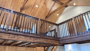 A wooden interior with a balcony railing, wooden beams, and recessed lighting. - Chalet Gedouque, a tranquille retreat located on the Cabot Trail with waterfront views (Chéticamp)