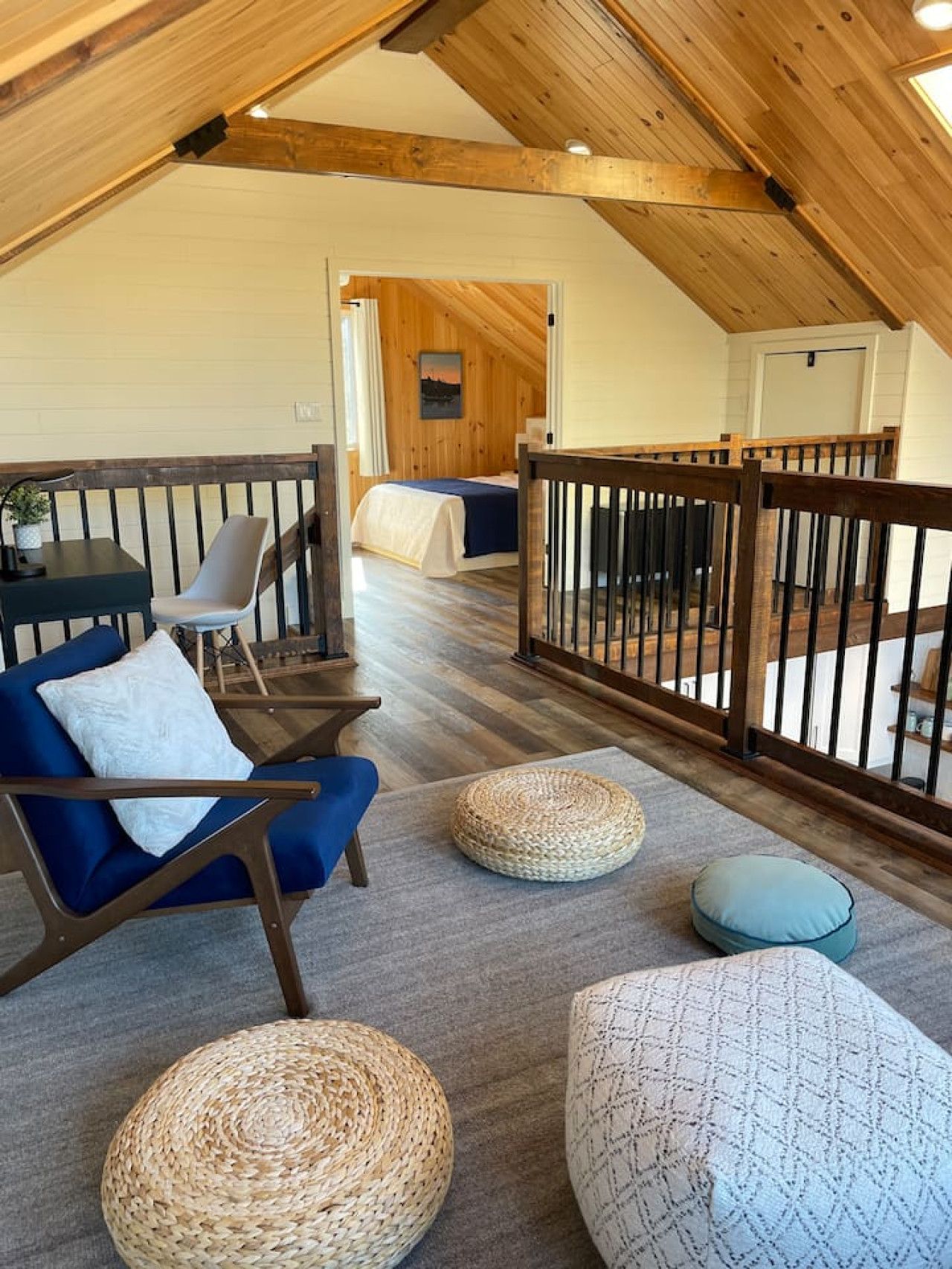 Ein Loft-Zimmer mit hohen Decken, Holzbalken, einem Balkon mit Geländer, einem Bett, einem Schreibtisch und einem Stuhl.