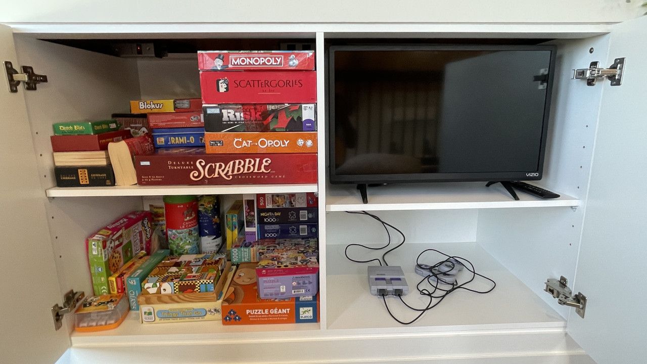 A storage unit with shelves containing various board games and a television.