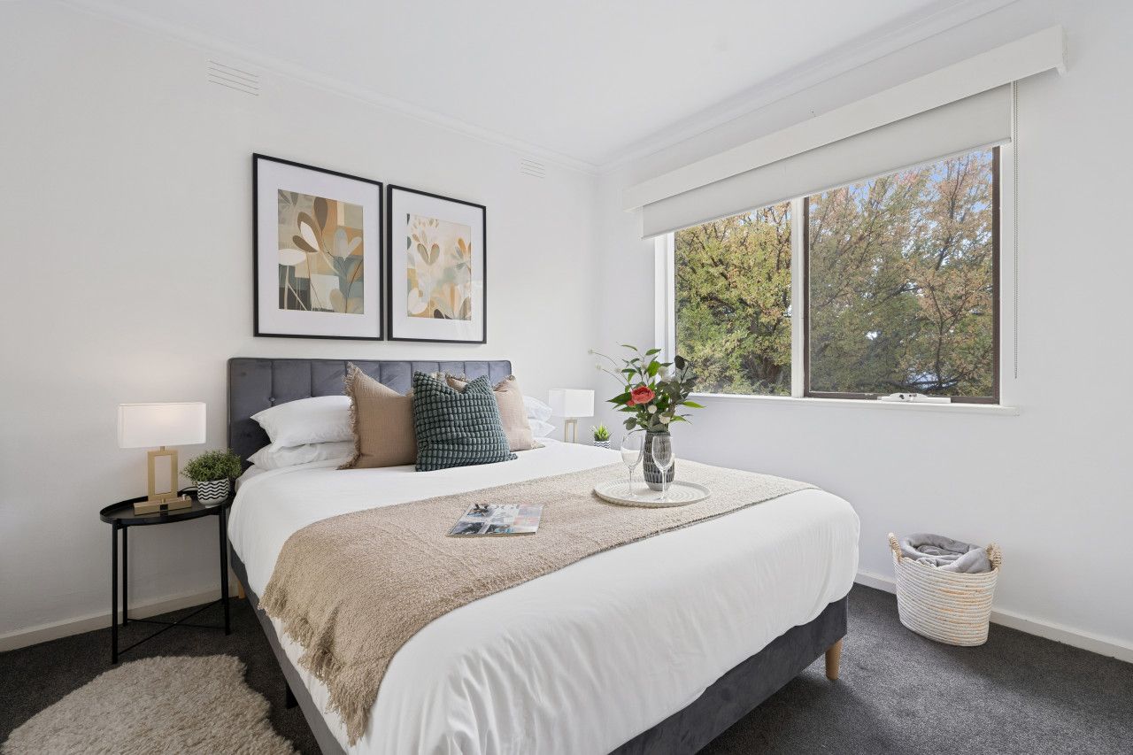 A bedroom with a bed, bedside tables, a window, and artwork on the wall.