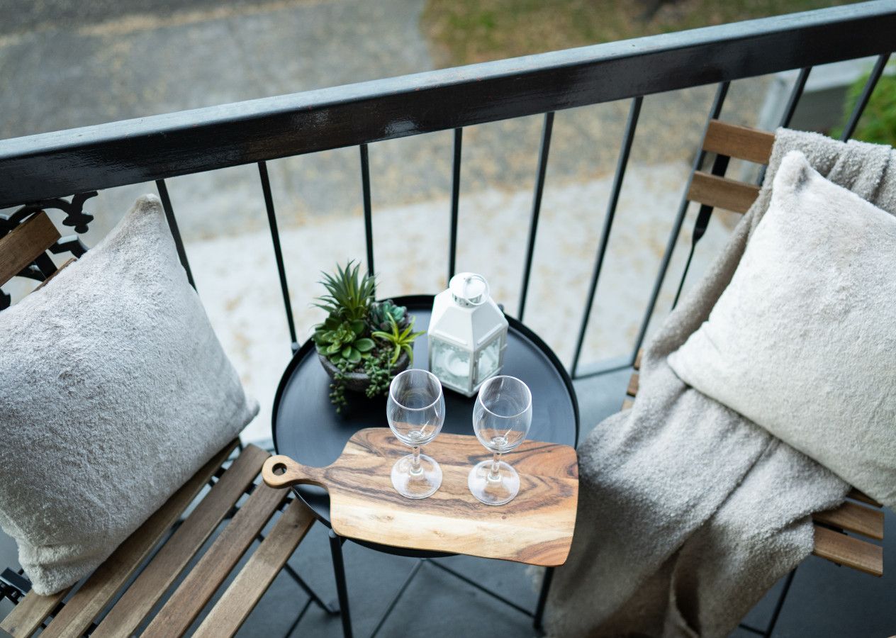 A balcony with a wooden chair, a small table with two glasses and a candle, and a potted plant.