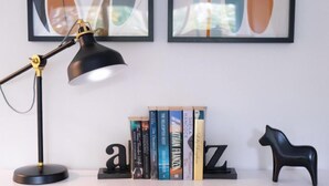 Una scrivania con una lampada da tavolo nera, una scultura a forma di cavallo nero e una libreria con libri.