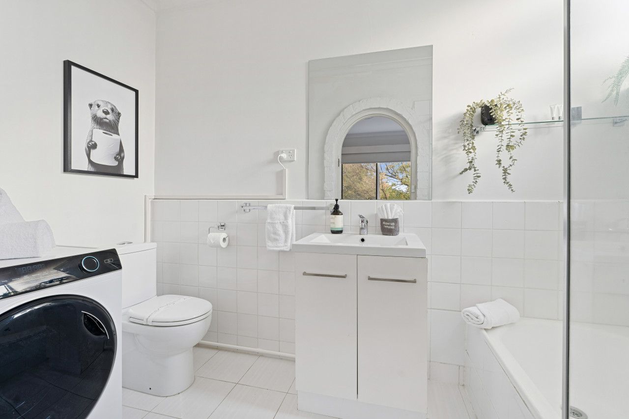A modern bathroom with a washing machine, toilet, sink, and shower.