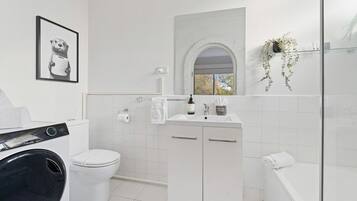 A modern bathroom with a washing machine, toilet, sink, and shower.