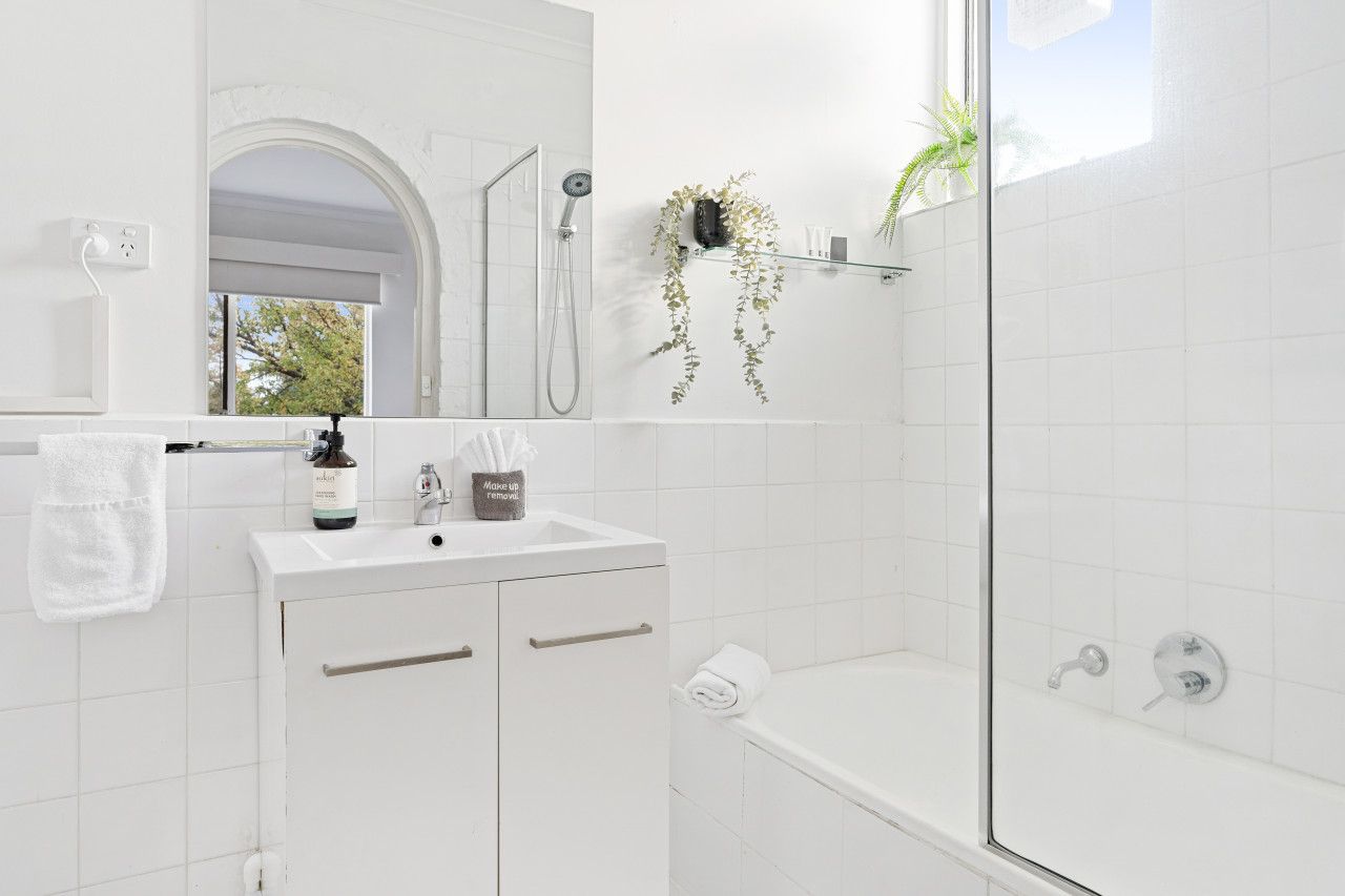 A modern bathroom with a glass shower enclosure, a white sink with a bottle of shampoo, and a towel rack.