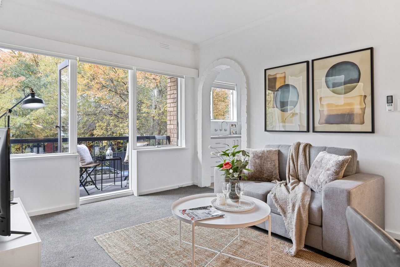 A modern living room with a grey sofa, a coffee table, and a large window offering a view of trees.