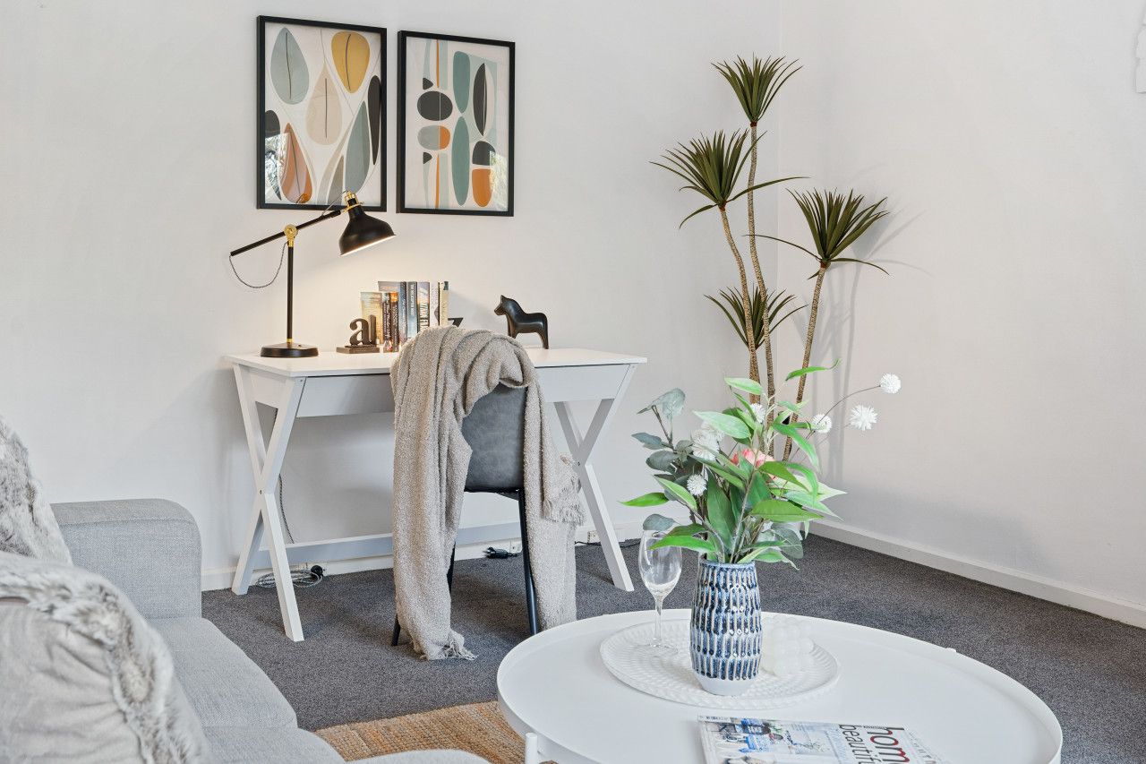 A modern living room with a white desk, a grey sofa, and a coffee table with a vase.
