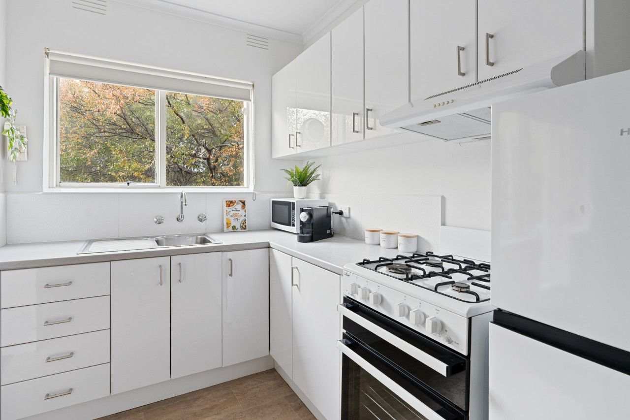 A modern kitchen with white cabinetry, a gas stove, a microwave, and a window with a view of trees.