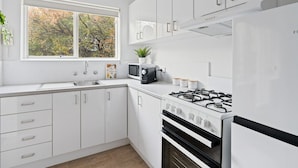 Una cucina moderna con mobili bianchi, un piano cottura a gas, un forno a microonde e una finestra vista alberi.